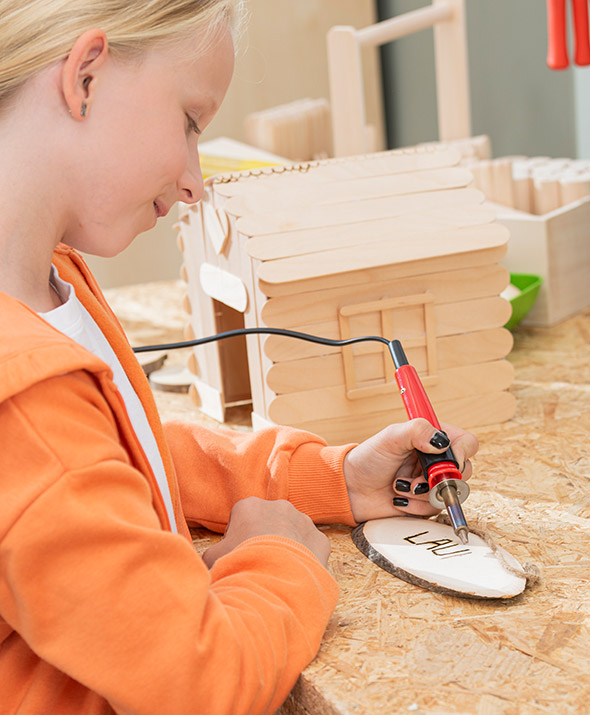 Schülerin erstellt ein Holzschild mit Namen