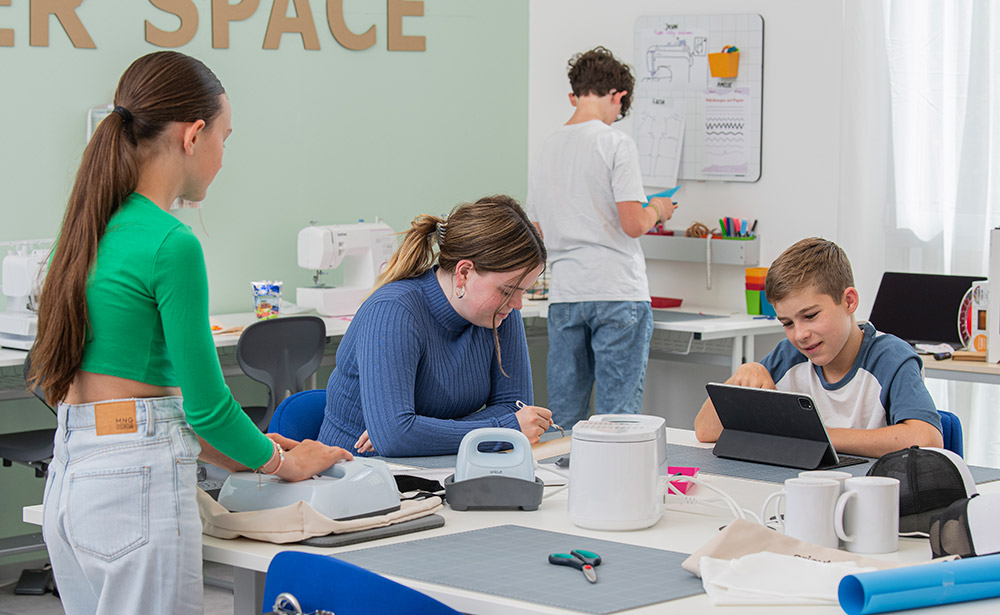 Mehrere Kinder an einem grossen Tisch und jedes Kind ist mit einem anderen Arbeitsschritt des Plotterns beschäftigt